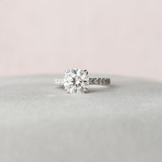 an engagement ring with a single diamond in the center on a white surface, against a light pink background