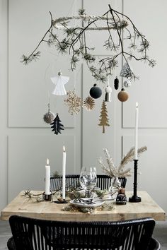 a dining room table decorated for christmas with ornaments hanging from the tree branch and candles