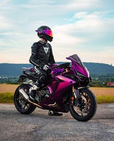 a person sitting on a purple motorcycle in the middle of a road with mountains in the background