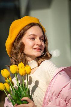 a woman in a yellow hat and coat holding some yellow tulips with her eyes closed