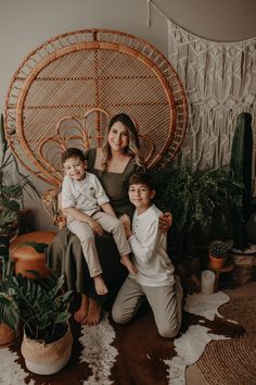 a woman and two children sitting on a wicker chair in front of a plant