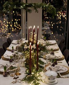 a table set for christmas dinner with candles and greenery