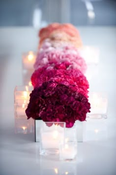 flowers in vases with candles on the side and lights behind them, all lined up