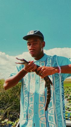 a man holding a small alligator in his hands while wearing a hat and blue shirt