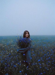 a woman standing in a field full of blue wildflowers with her arms wrapped around her body