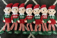 seven elf dolls are lined up on the carpet in their green and red christmas outfits