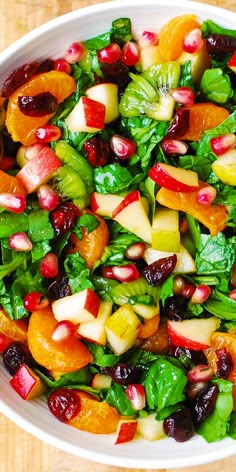 a white bowl filled with spinach, oranges and cranberry salad on top of a wooden table