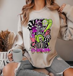 a woman wearing a sweater with the image of two clowns on it and holding a coffee mug