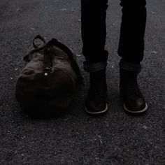 a person standing next to a duffel bag on the ground with their legs crossed