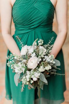 a woman in a green dress holding a bouquet of white flowers and greenery on her wedding day