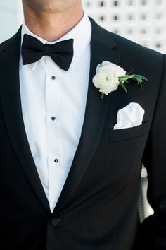 a man wearing a black tuxedo with white flowers on the lapel and bow tie