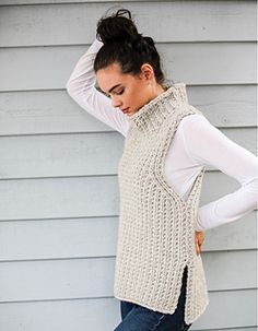 a woman leaning against a wall wearing a sweater vest