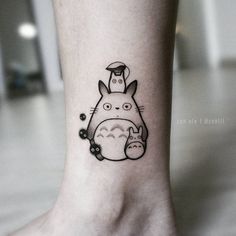 a small tattoo on the ankle of a person with a totoro head and flowers