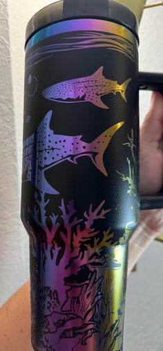 a hand holding a colorful coffee cup with fish on it