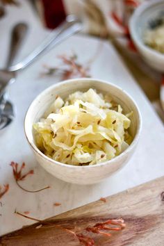 a white bowl filled with coleslaw on top of a wooden cutting board next to spoons