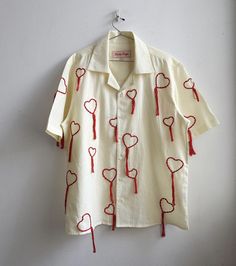 a white shirt with red thread on it and hearts drawn on the front, hanging from a hanger