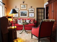 a living room with red couches and pictures on the wall above them, along with two chairs