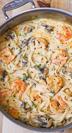 a pan filled with pasta and shrimp on top of a wooden table