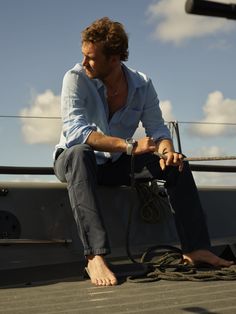 a man sitting on the deck of a boat with his hands in his pockets and looking off into the distance