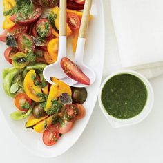 a white plate topped with lots of different types of vegetables next to a bowl of pesto