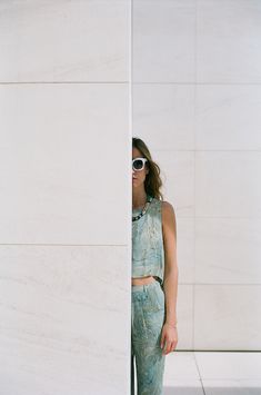 a woman standing in front of a white wall with sunglasses on her head and wearing green pants