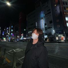 a woman wearing a face mask standing on the side of an empty street at night