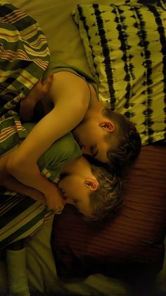 two children are sleeping on a bed with green and black sheets, one boy has his head on the pillow