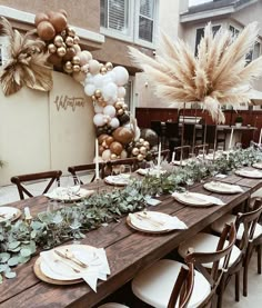 a long wooden table topped with lots of plates and place settings covered in greenery