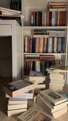 a pile of books sitting on top of a wooden floor next to a book shelf