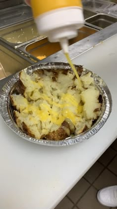 someone is pouring cheese on top of food in a tin foil pan at a counter