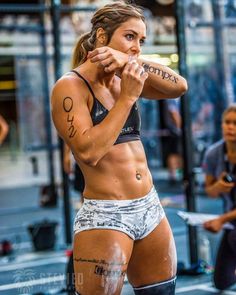 a woman with tattoos on her arm and chest standing in front of a gym floor