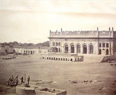 an old black and white photo of a building in the middle of a field with people standing around it