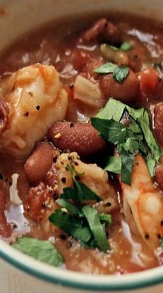 a close up of a bowl of food with shrimp and beans in it on a table