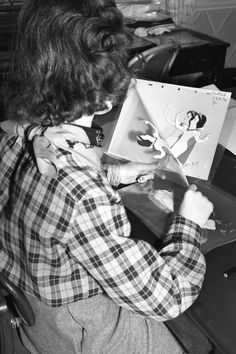 a woman sitting at a desk drawing on a piece of paper