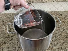 a person pouring something into a pot on the stove top with a measuring cup in it