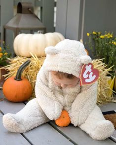 a small child in a white teddy bear costume sitting on a porch with pumpkins and hay