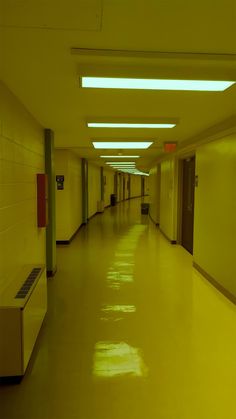 an empty hallway with yellow walls and flooring is lit by recessed lights on the ceiling