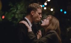 a man and woman standing next to each other in front of christmas lights with their noses close together