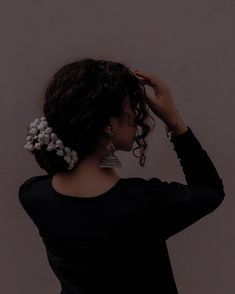 a woman with curly hair wearing earrings and a black shirt is looking off into the distance