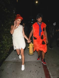 a man and woman in costumes walking down the street at night with fire hydrant