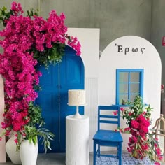 a blue chair sitting in front of a white building with pink flowers growing out of it