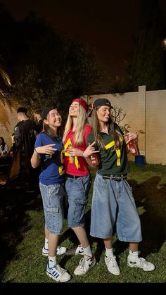 three young women standing next to each other on top of a grass covered field at night