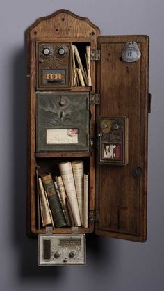 an old wooden box with many items inside it on a gray wall next to a clock