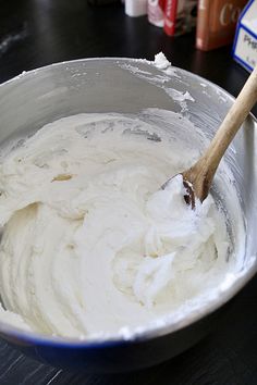 a mixing bowl filled with white batter and a wooden spoon in it on top of a table