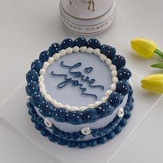 a blue and white cake sitting on top of a table next to tulips