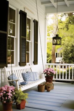 a porch swing with flowers and potted plants on the front porch next to it