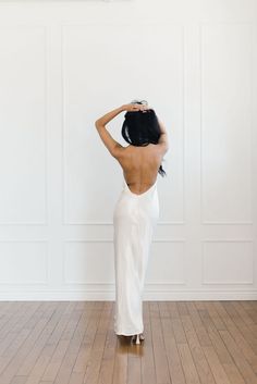 the back of a woman in a white dress standing on a hard wood floor with her hands behind her head