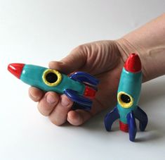 two toy rockets in the palm of a hand on a white surface with one being held by another