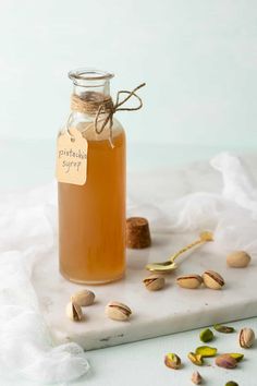 a glass jar filled with liquid sitting on top of a white counter next to nuts