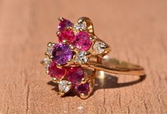 The Hempstead Bubblegum Ruby & Diamond Cocktail Ring. The ring features a reddish purple sapphire center stone with vivid red natural rubies and pink sapphires cascading from the center. Mixed between are diamonds throughout. The ring contains approximately 2 carats total weight by measurement of rubies and sapphires. The total estimated diamond weight by measurement is 0.36 carats. The ring is crafted in 14 karat yellow gold and is currently a finger size 6 yet can be adjusted to any finger Red Multi-stone Sapphire Ring, Pink Oval Multi-stone Ruby Ring, Pink Lab-created Ruby Ring, Pink Ruby Ring With Gemstone Accents For Anniversary, Multi-stone Cluster Ruby Ring, Multi-stone Ruby Cluster Ring, Pink Multi-stone Amethyst Ring, Formal Multi-stone Pink Ruby Ring, Formal Pink Multi-stone Ruby Ring